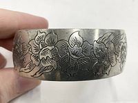 Close-up of pewter cuff bracelet showing engraved daffodil flowers wrapping around the band
