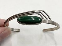 Close-up of bracelet showing the malachite stone and sterling silver band design held by a hand.