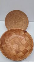 Two wooden salad bowls: one woven style and one spiral design, side by side on surface.