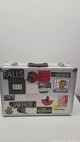 Front side of aluminum instrument case with multiple varied stickers and latch locks visible.