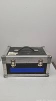 Closed aluminum instrument case with black handle, two lockable silver latches, black exterior with blue panel on front and metal corner protectors.