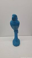 Front view of blue plastic parrot decor on a white surface with visible wear and chipping.