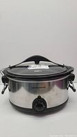 Front view of silver stainless steel Hamilton Beach slow cooker with clip-tight black lid and dial control, showing condition and branding.