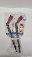 Two new adjustable basting brushes in original sealed plastic packaging with black handles and red silicone heads positioned on a white background.