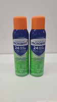 Front view of two Microban 24 Hour Sanitizing Spray cans side by side showing label and orange caps.