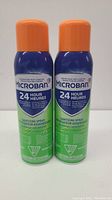 Front view of two Microban 24 Hour Sanitizing Spray cans, 425g each, with orange caps and blue-green labels.