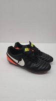 Pair of black Nike Tempo men's soccer cleats showing side profile with white swoosh and orange accents.