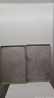 Two rectangular metal baking trays, one solid and one perforated, placed side by side against white background.