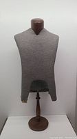 Front view of Taylor mannequin torso on wooden base showing gray fabric cover with damage near bottom and head piece.