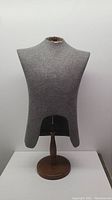 Front view of grey fabric-covered mannequin torso mounted on round oakwood base, showing shape and fabric condition including worn neck area.