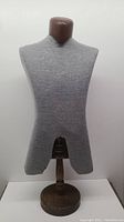 Front view of gray fabric-covered tailor's mannequin torso on round solid oakwood base showing front cutout for shirt fitting.