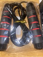 Jump rope with black padded handles with red stripes, coiled and tied with yellow twist tie, plastic wrapped.