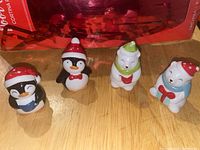 Image of two penguin and two polar bear salt and pepper shakers arranged on a wooden surface under red wrapping paper.