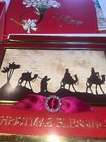 Photo of a red Christmas card with a black silhouette nativity scene, pink ribbon with rhinestone detail, and gold text reading 'Christmas Blessings'