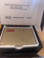 Top view of vintage Labelon metal stamp press inside box with patent info on lid