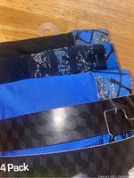 Three pairs of boys boxer briefs, black, blue, and blue with black pattern, with ripped packaging visible in the background.