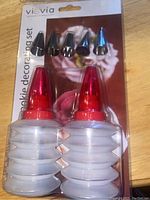 Photo of cookie/cupcake decorating set in packaging showing two white squeeze bottles with red caps and five metal icing tips.