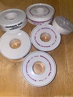 Photo showing five rolls of waterproof adhesive tape in a plastic container and one refill roll wrapped in paper, all white rolls each labeled 1/2 inch by 10 yards.