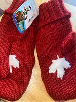 Close-up of the red mittens showing white maple leaf applique and knit texture