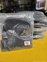 Photo shows a stack of 10 black knit toques, each individually packaged in clear plastic bags. The toques have a ribbed knit texture and folded cuffs.