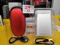 Image of 3 handwarmers: two large silver portable handwarmers with USB cables and one red handwarmer, all in clear plastic packaging.