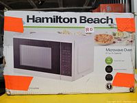 Box of Hamilton Beach microwave oven showing the brand, product image, and key specifications such as 0.7 cu.ft. capacity and 700 watts power.