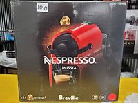 Photo of the Breville Nespresso Inissia espresso machine packaging box, showing red color model and branding details.
