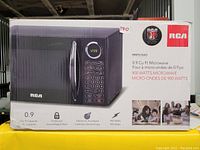 Photo of packaged RCA microwave oven box showing product image, features, and branding.