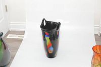 Tall black blown glass vase with colorful abstract layers and cut-out handled irregular rim, shown from front angle.