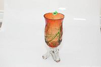 Full view of the orange and green blown glass vase with clear base on tripod-like feet.