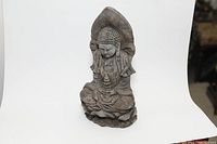 Front view of the seated stone Buddha statue showing detailed face, hands in prayer pose, and draped robes.