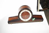 Front view of the 1930s wooden mantel clock showing circular clock face inside a wooden rounded hood and rectangular base.