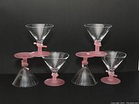Four handmade glass ice cream goblets. Clear conical bowls with pink stems and bases, shown against a black background.