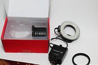 Aputure Amaran Macro LED ring light with power cord, 10 lens adapters, and original box open showing lens adapters.