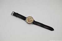 Photo of automatic mechanical wrist watch with visible skeleton dial and black leather strap laid flat.