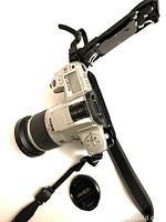 Silver Minolta 35mm film camera with attached zoom lens and black strap, lens cap visible to the side.