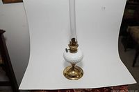 Photo of the vintage white milk glass oil lamp with brass base and chimney against a white background.