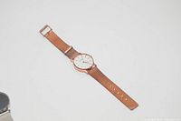 Photo of a rose gold wrist watch with a white face and mesh band laid flat on a white surface.