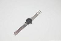 Photo of a silver wristwatch with a mesh band laid flat on a white surface, showing the entire watch including the dial and strap.