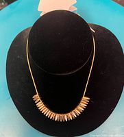 Gold necklace displayed on black velvet bust showing slender chain with multiple elongated teardrop pendants.