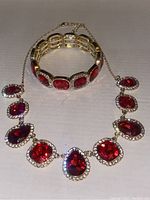 Necklace and bracelet set on flat surface showing red stones and clear halos