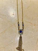 Photo of the 22 inch gold chain necklace with pendant featuring an oval central blue tanzanite surrounded by smaller blue stones and a gold chain tassel.