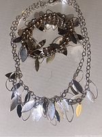 Photo shows silver-tone necklace and bracelet with leaf-shaped charms arranged on a white surface.