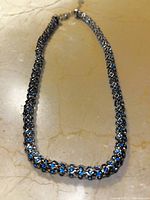 Photo of a blue stone necklace with silver-tone metal chain laid out flat on a surface.