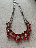 Silver chain necklace with red flower charms featuring clear crystals on a light surface.