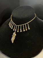 Image showing gold-tone necklace with bead dangles and a larger leaf-shaped pendant with clear stones, displayed on black velvet stand.