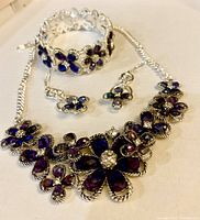 Photo of necklace, bracelet, and earrings set showing purple flower stones and silver-toned metalwork.
