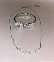 Photo shows silver-tone bangle bracelet and matching necklace with white enamel flower decorations and rhinestone centers.