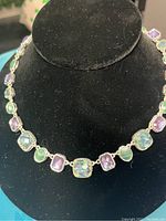 Photo of a silver-tone necklace with alternating amethyst and erinite square stones displayed on a black necklace stand.