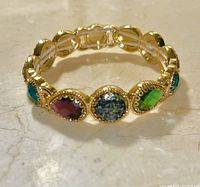 Front view of gold-tone bracelet with various colored oval stones including garnet, green topaz, and a multicolored stone.